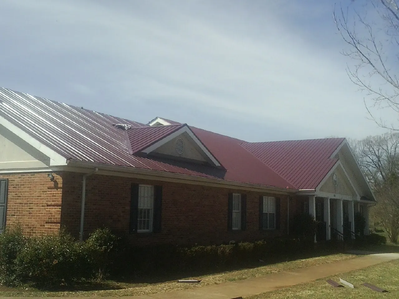 Red metal roof with gabled entries on a long brick building, from a Hail Damage Roof Repair job in Almont