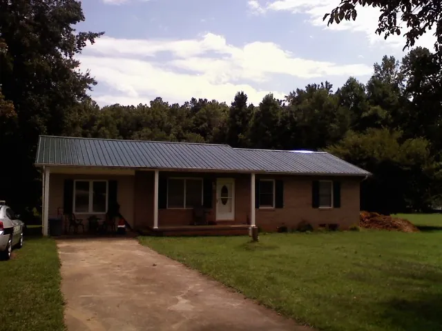 Dark green metal roof on a brick ranch with a covered porch in Almont