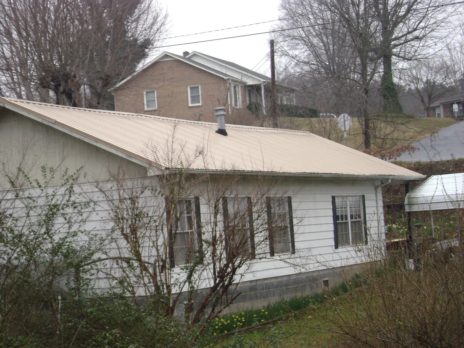 Tan metal roof on a white sided house set into a hillside — Commercial Roofing by Roofing Brothers in Almont